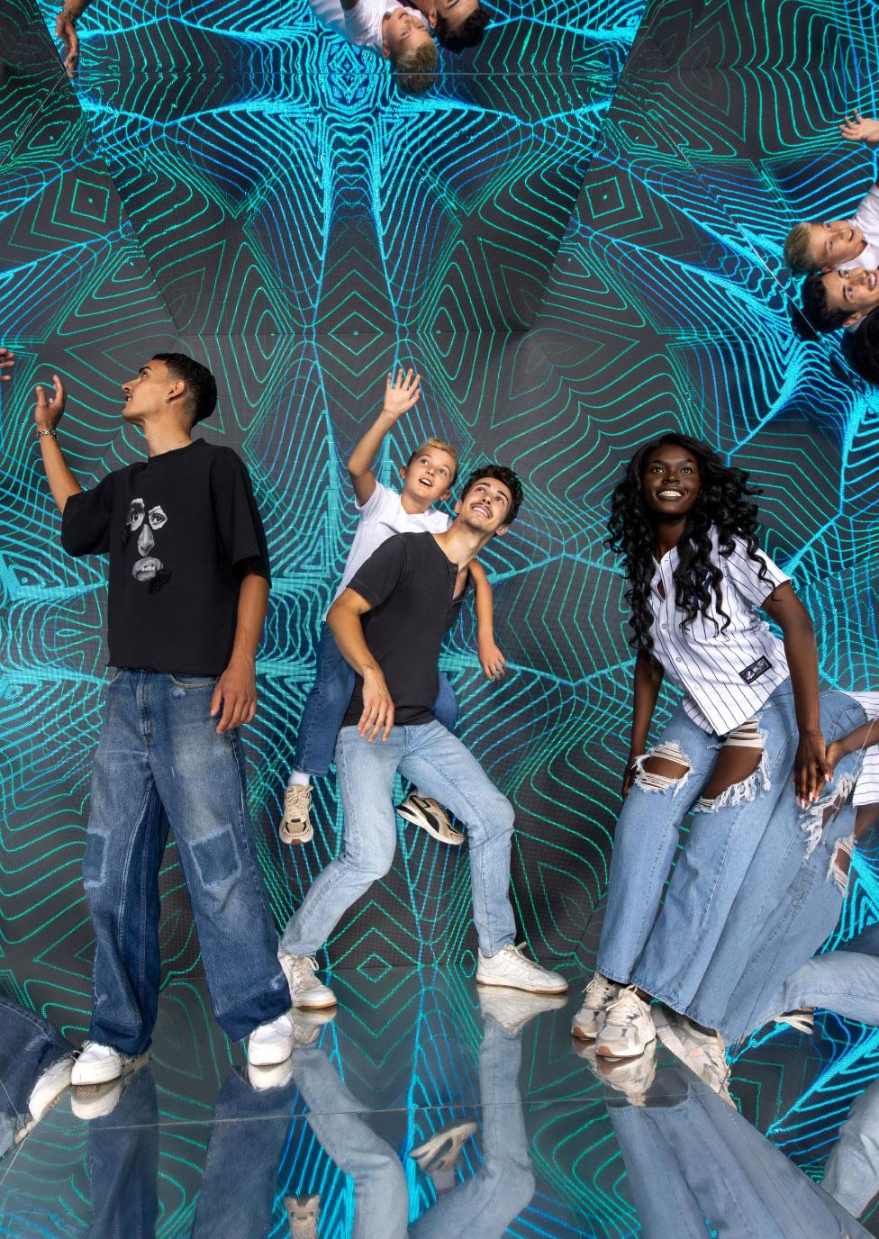 Visitors interacting in an immersive illusion room with mirrored floor reflections and repeating blue geometric patterns at the Museum of Illusions.